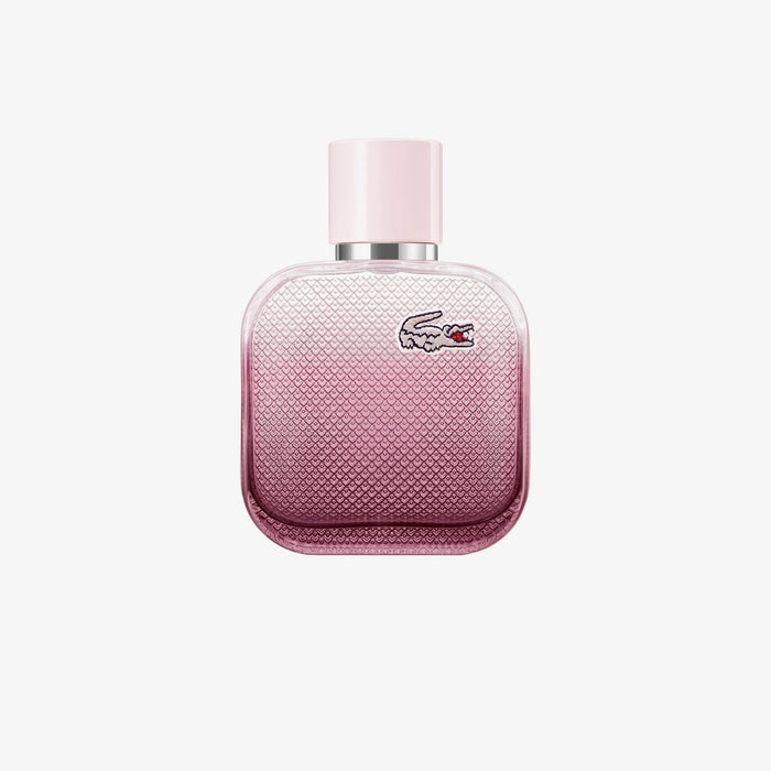 Bottle of L.12.12 Rose Eau Intense perfume with floral elements like rose, iris, cotton flower, and cedarwood in the background
