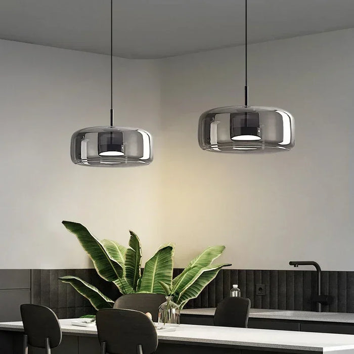 Nordic-style smoky gray and amber glass pendant light hanging over a modern dining table with soft warm lighting