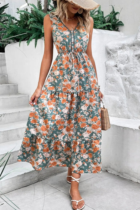 Woman wearing a floral V neck sleeveless dress with a tie waist and tiered hem – perfect for summer.