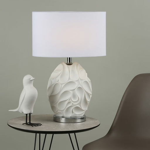 Zachary table lamp with sculptured oval matt white base, polished chrome details, and oval off-white linen shade

