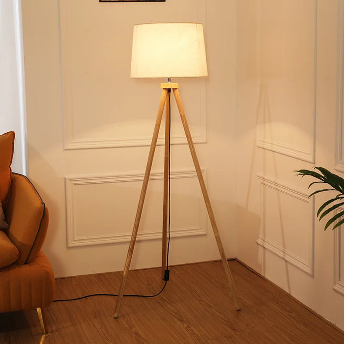 Mid-century modern tripod floor lamp with natural rubber wood legs, beige fabric shade, and foot switch control for stylish home lighting

