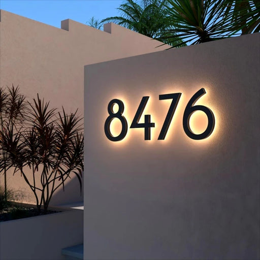 Backlit stainless steel LED house numbers mounted on an outdoor wall at night