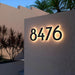 Backlit stainless steel LED house numbers mounted on an outdoor wall at night