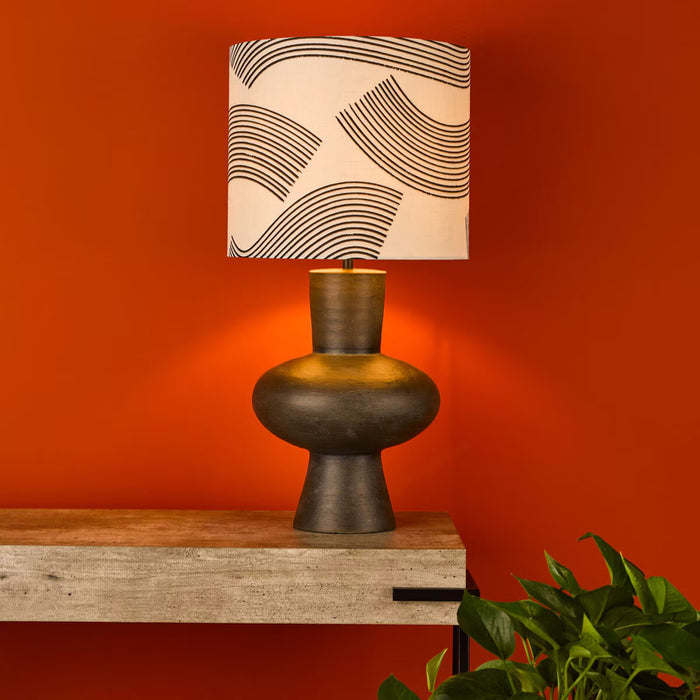  table lamp with bulbous resin base and patterned linen and black fabric shade on side table

