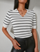 Woman wearing a black and white striped V-neck top with short sleeves and contrast collar, styled with jeans for a chic everyday look.