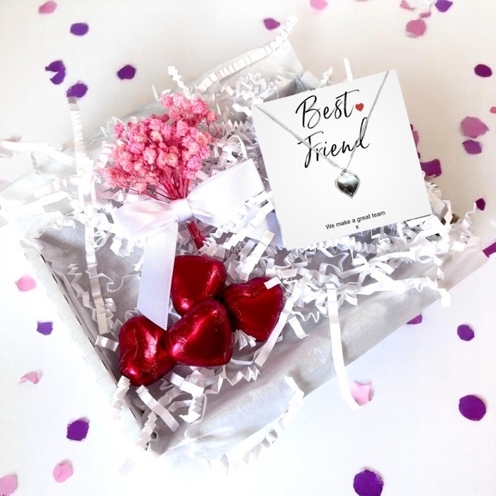 Elegant letterbox friendly mini gift hamper containing a silver heart necklace on a message card, four red foiled chocolates, and a mini bouquet of dried white flowers.