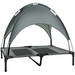 Small to medium dog relaxing on an elevated grey pet lounger with canopy, outdoors on grass


