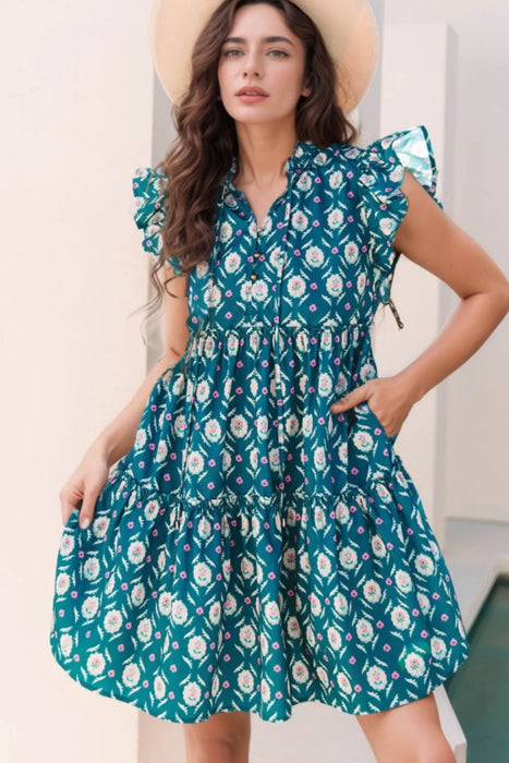 Model wearing a printed tie neck ruffled cap sleeve dress with frill details in a light and elegant summer design