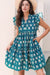 Model wearing a printed tie neck ruffled cap sleeve dress with frill details in a light and elegant summer design