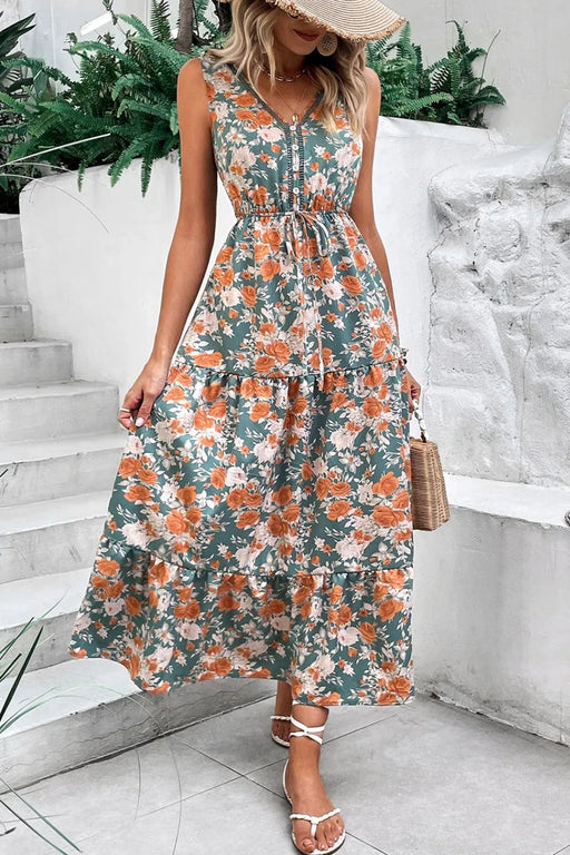 Woman wearing a floral V neck sleeveless dress with a tie waist and tiered hem – perfect for summer.